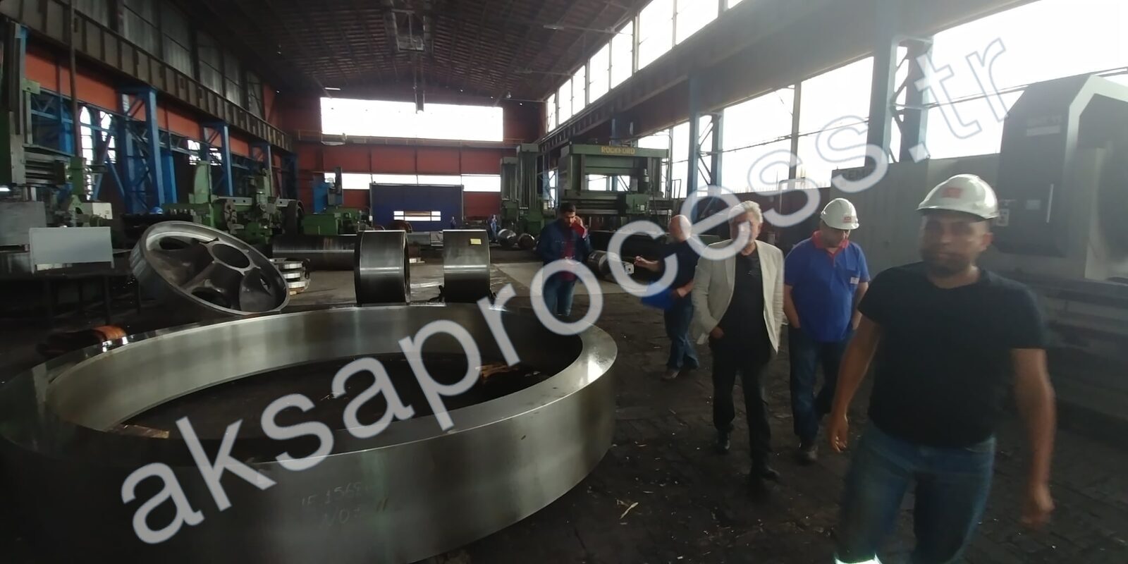 Our founder and team in a heavy machine shop alongside a large machined grinding ring and mill rollers